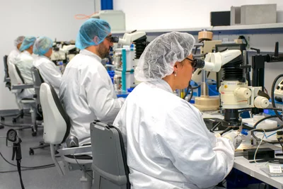 Microscope-assisted manual assembly process performed by operators in a manufacturing environment.