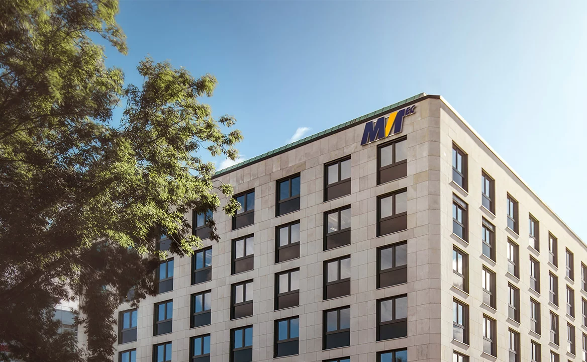 Modern office building with MVTec logo on the roof edge, photographed under blue skies and framed by trees.