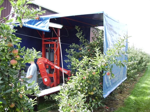 Robotic apple harvester picking apples in an orchard with a canopy to control lighting conditions.