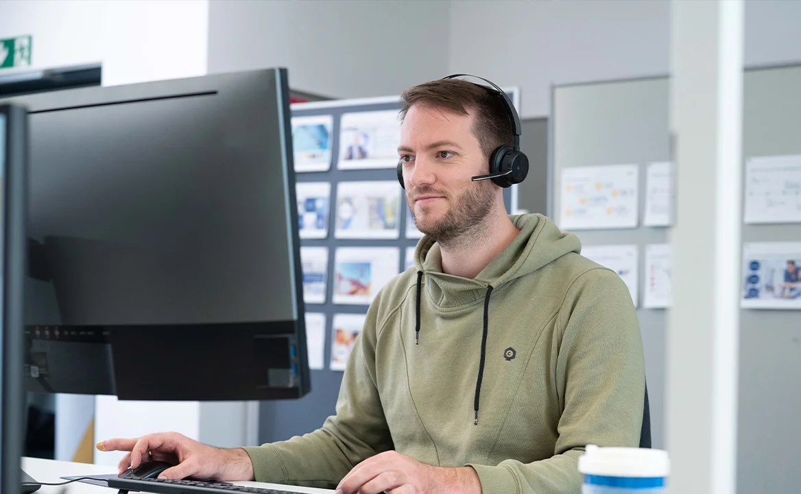 Technical support specialist wearing a headset, working at a desktop computer in an office environment.
