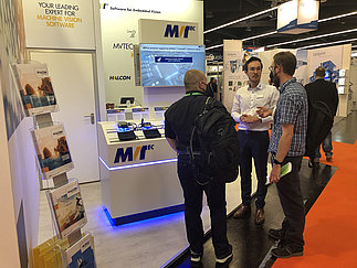 An MVTec expert talks to interested parties at the MVTec booth at embedded world 2022.